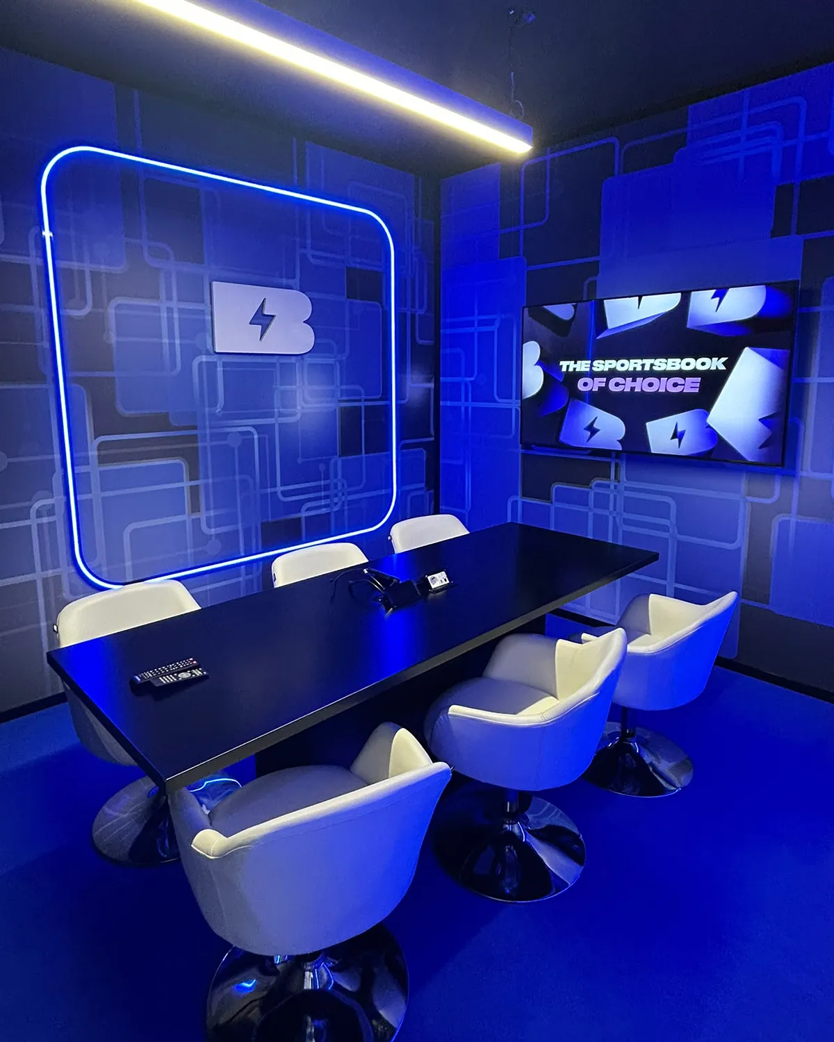 BETBY’s private meeting room at SBC Summit Lisbon, with blue illuminated branding, a black meeting table, white chairs and a wall-mounted screen.