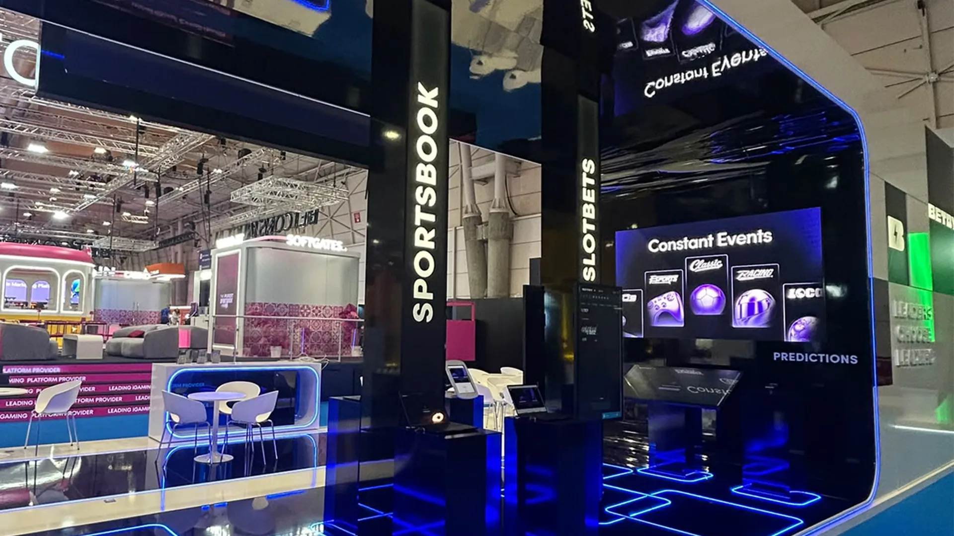 BETBY product demonstration area with Sportsbook and SlotBets signage, digital displays and blue illuminated flooring.