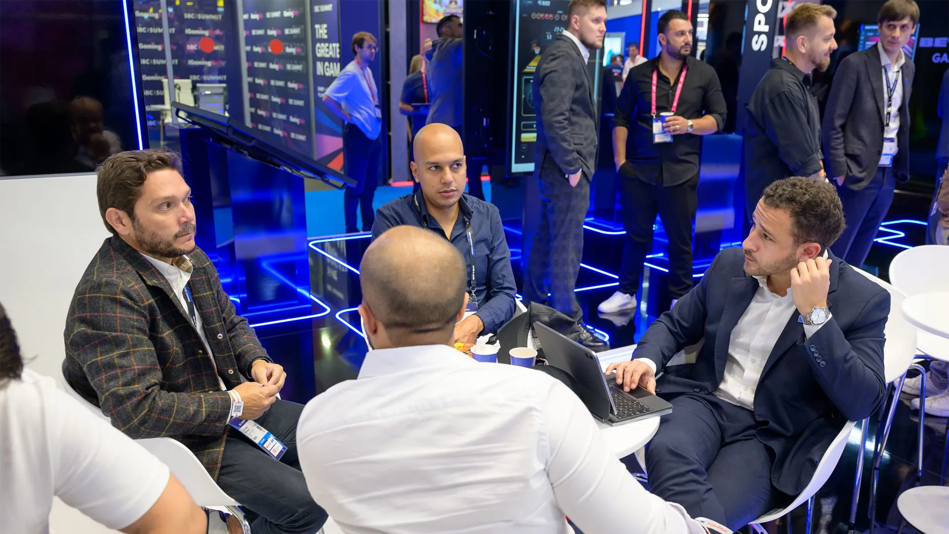 Attendees in a seated meeting around a small table with a tablet, beside BETBY’s illuminated product area.