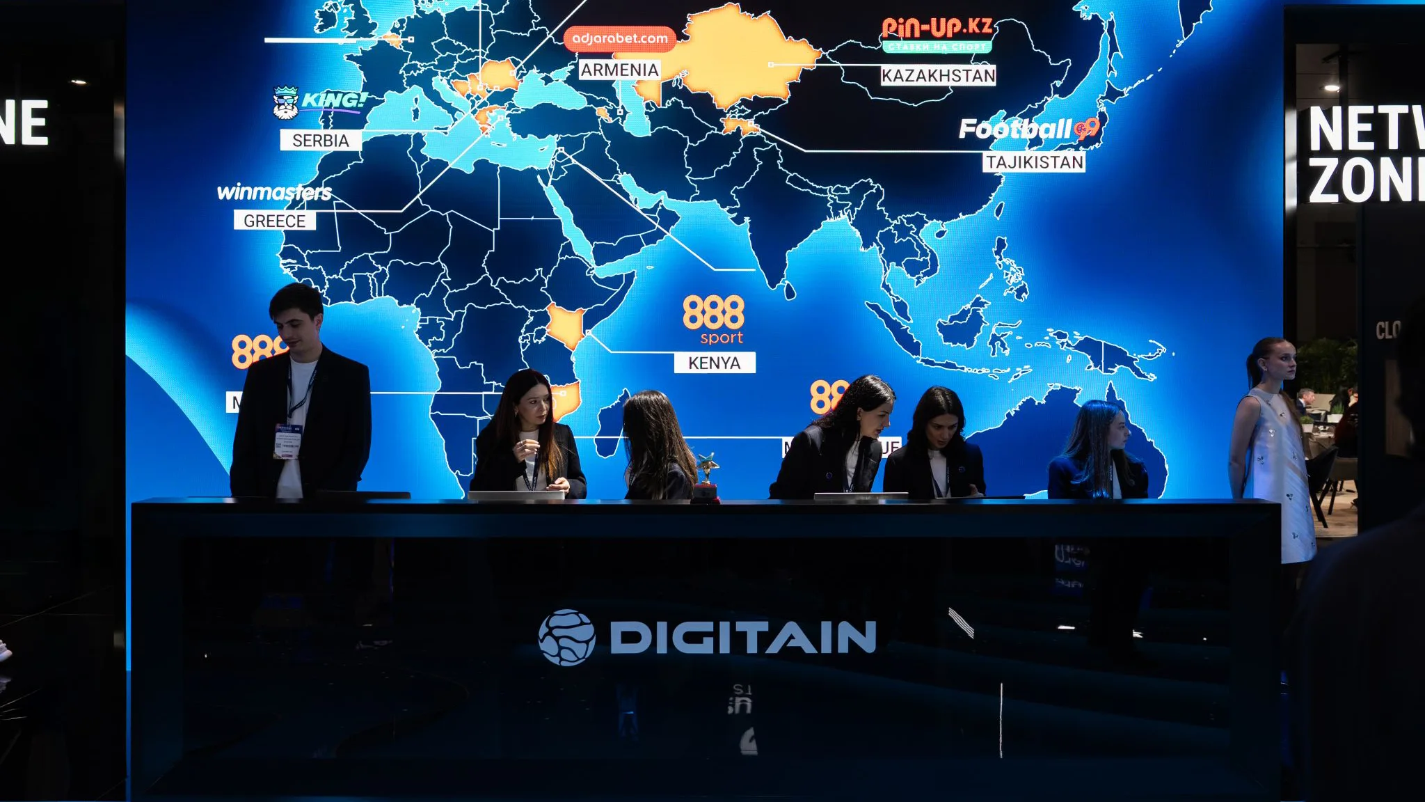 Digitain reception counter in front of a giant world map LED wall showing partner regions and brand logos.
