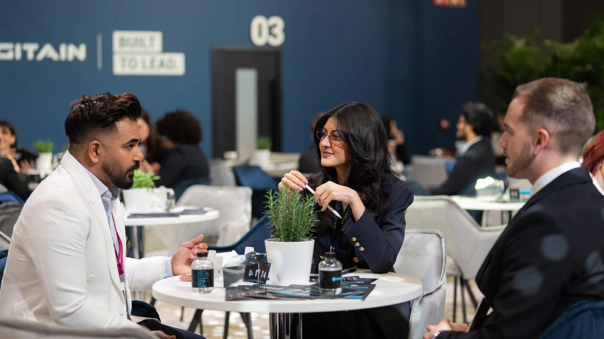 Three attendees in conversation at a round table in the Digitain lounge, with brochures and drinks on the table.