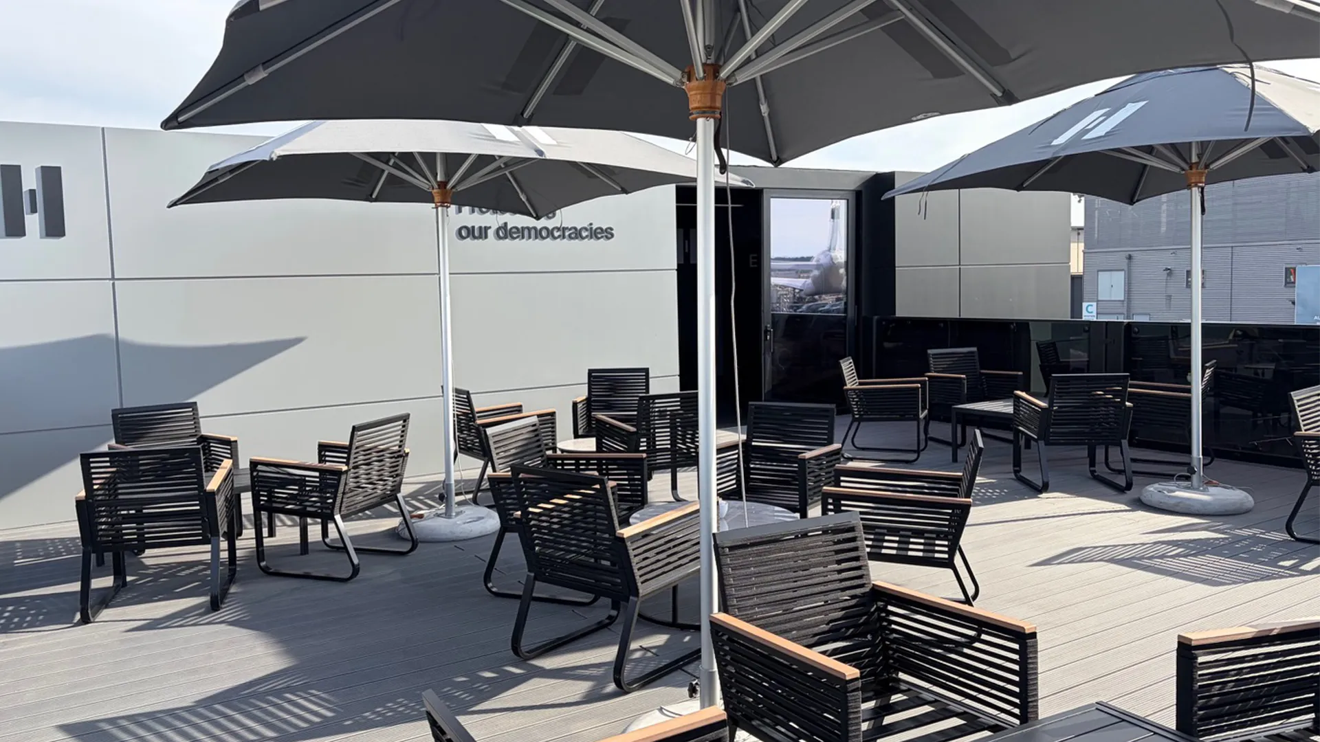 Outdoor hospitality terrace at Helsing’s ILA Berlin 2026 chalet with black seating and branded parasols