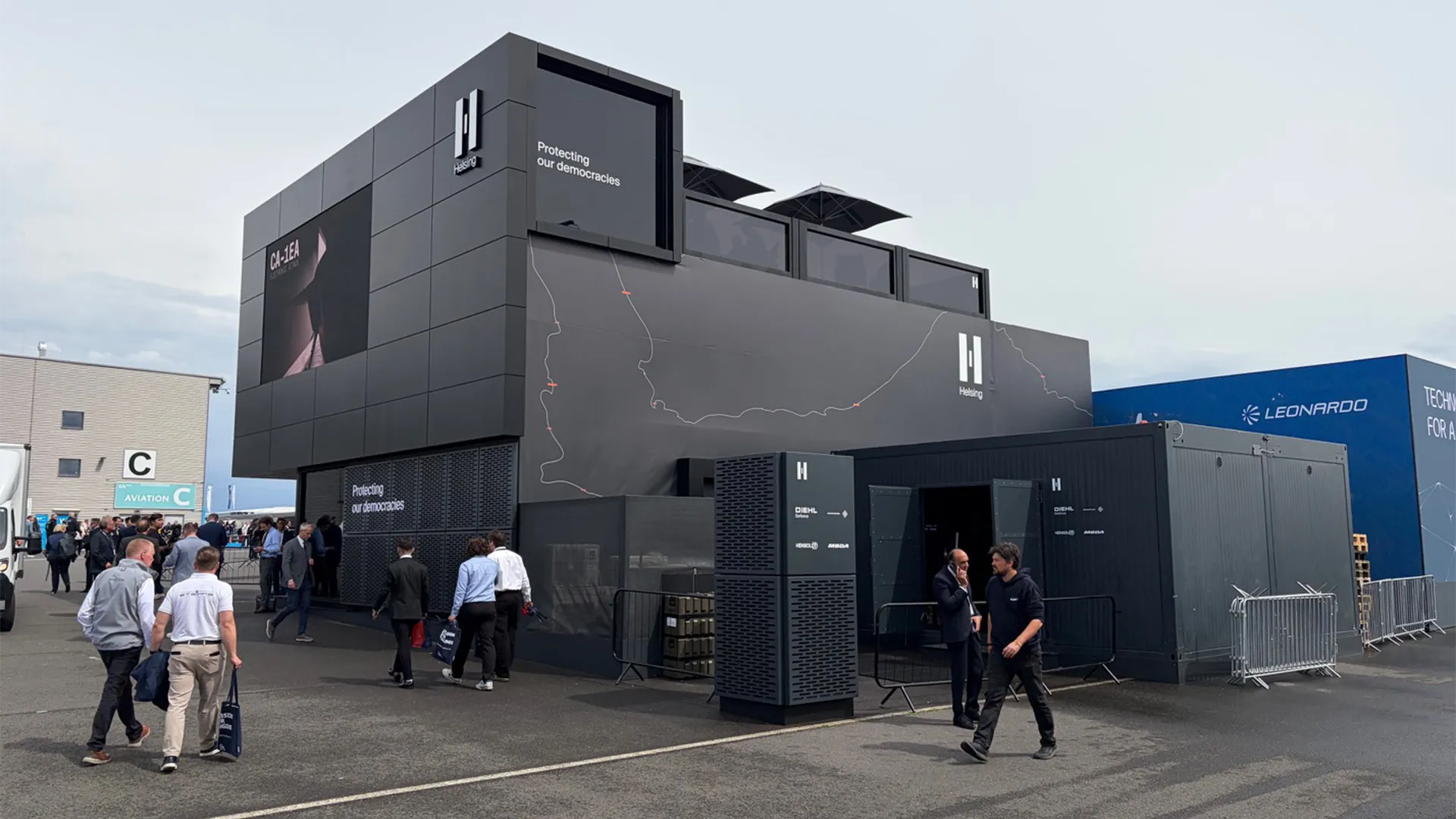 Rear exterior of Helsing’s chalet at ILA Berlin 2026 with branded partner units and arriving visitors