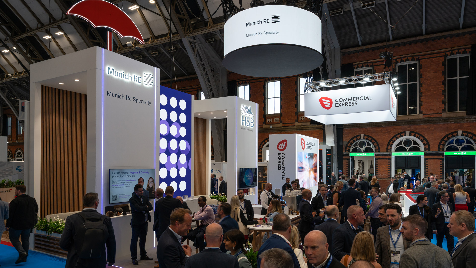 Munich Re Specialty and HSB exhibition stand at the BIBA Conference 2026, featuring illuminated branding, overhead circular signage and busy visitor engagement at Manchester Central.