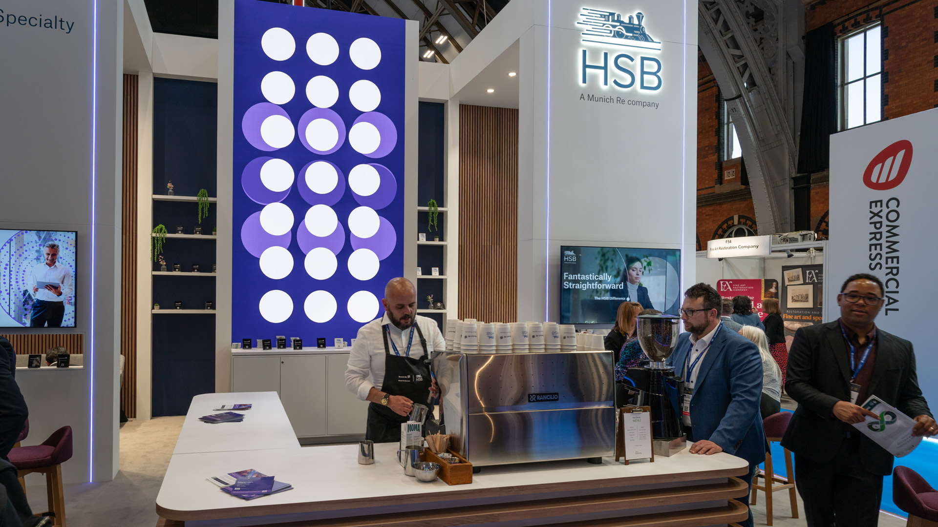 Barista service on the Munich Re Specialty and HSB exhibition stand at BIBA 2026, with branded digital content, hospitality counter and premium stand design details.